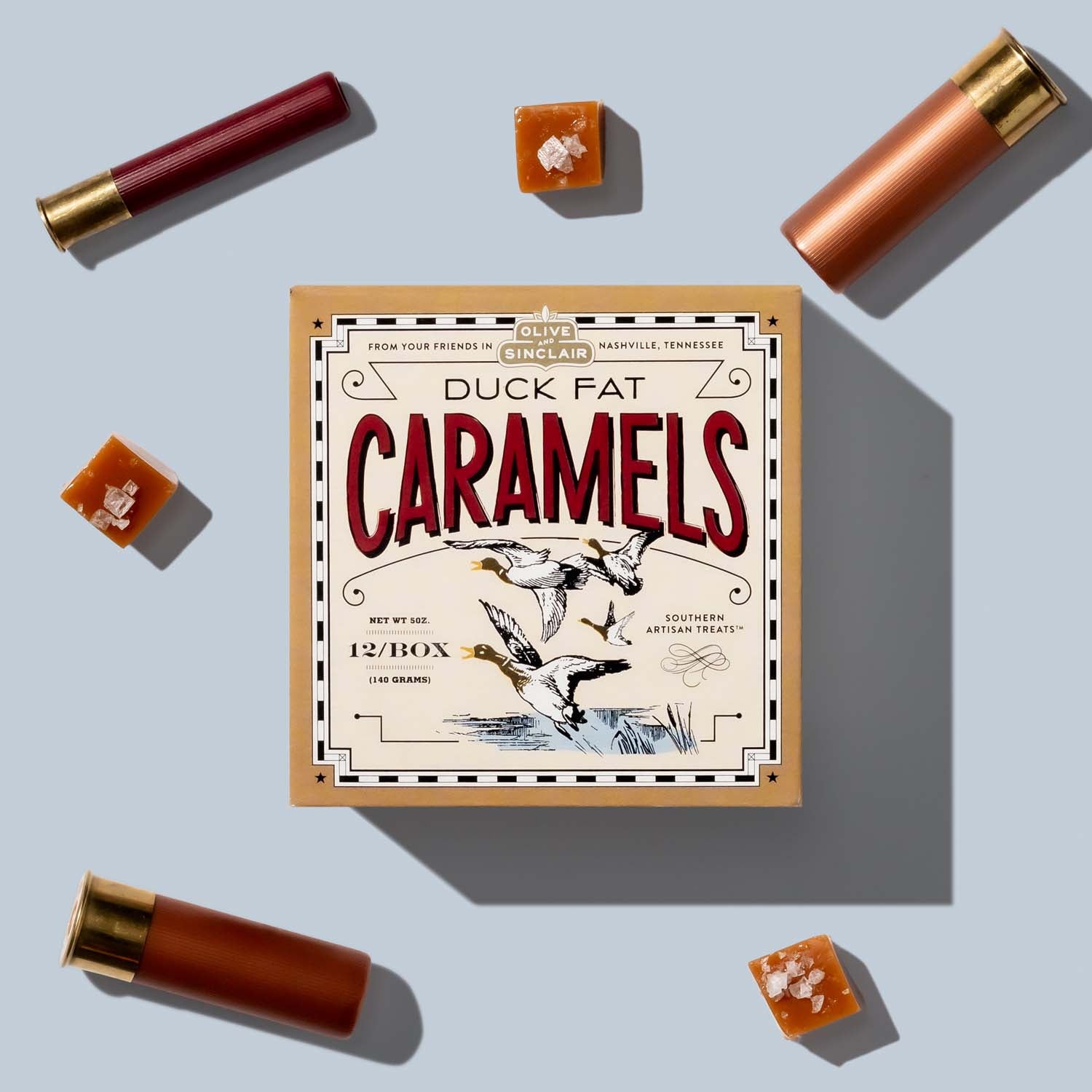 Box of Duck Fat Caramels with caramels around on a light blue background