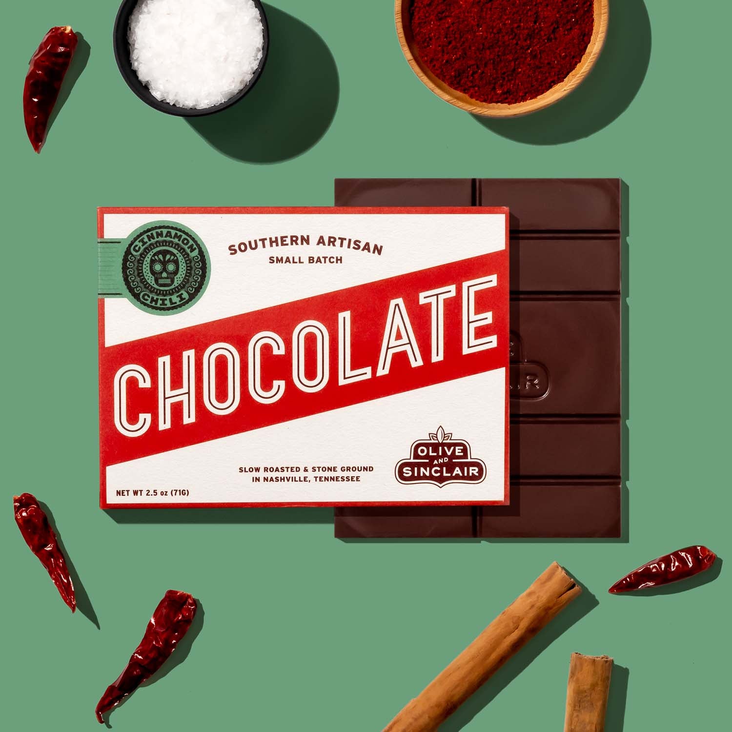 Olive and Sinclair Cinnamon Chili chocolate bar with cinnamon sticks and peppers in the background 