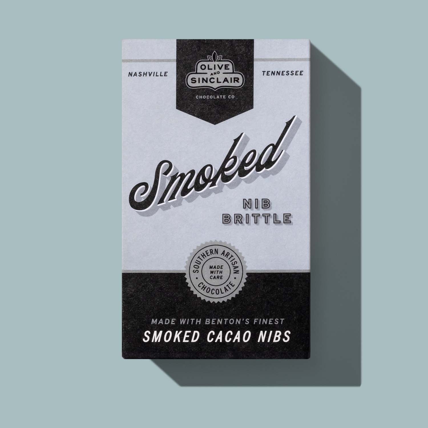 Packaging of Olive Sinclair Chocolate Co. Smoked Nib Brittle on a light blue background