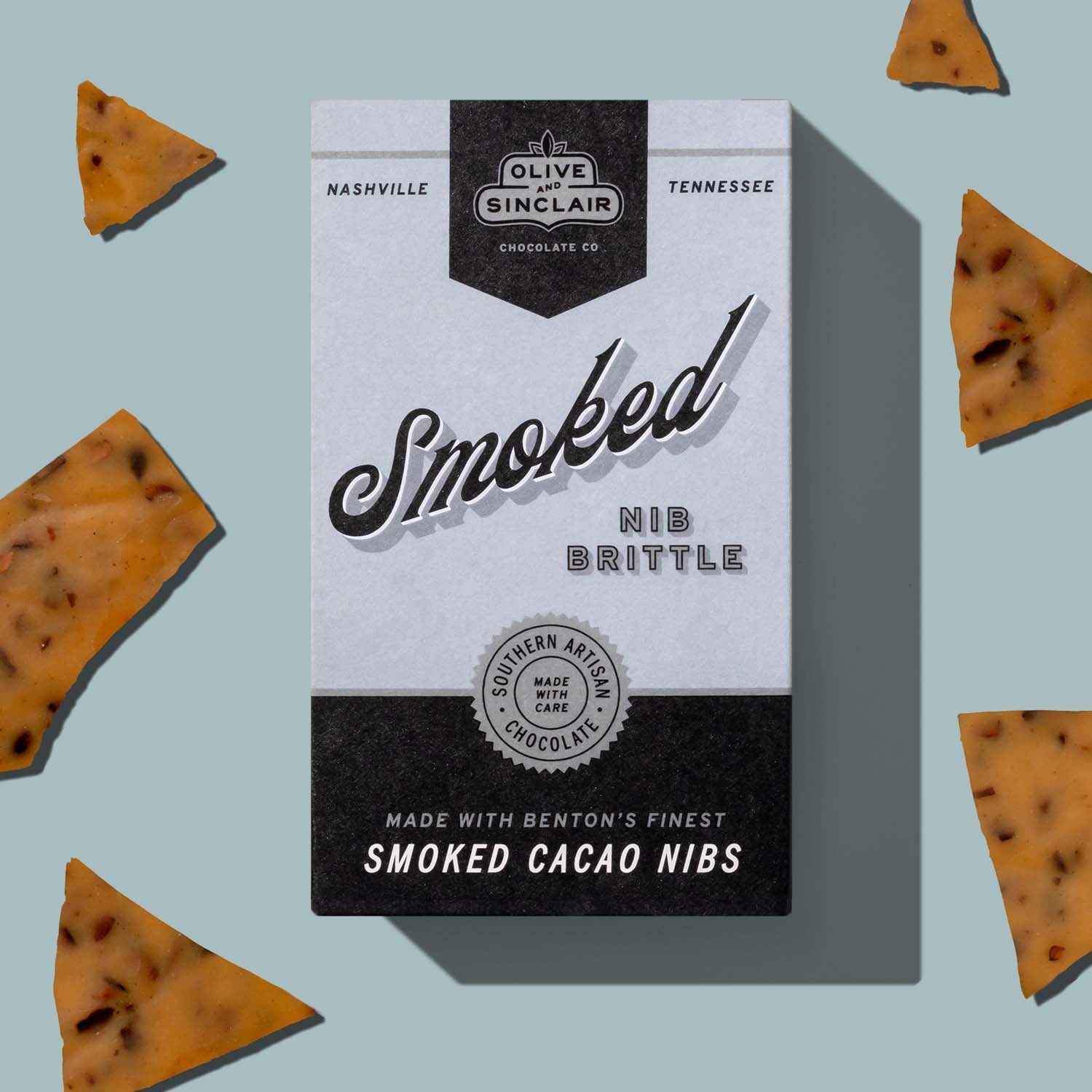 Olive Sinclair Chocolate Co. Smoked Nib Brittle packaging with brittle pieces on a light blue background